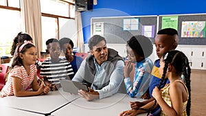 Diverse male teacher using digital tablet teaching children in class at elementary school