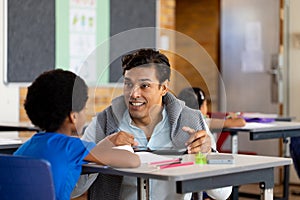 Diverse male teacher using tablet teaching children at desks in elementary school class