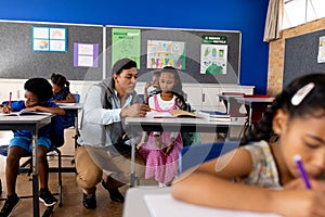 Diverse male teacher using tablet teaching children at desks in elementary school classroom