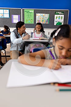 Diverse male teacher using tablet teaching children at desks in elementary school classroom