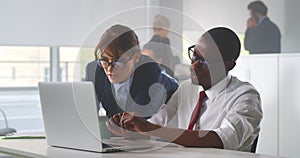 Diverse man and woman working together in creative office using laptop