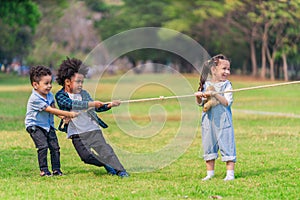 Diverse mixed race kids playing pulling rope together in park during summer