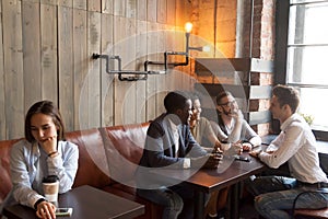 Diverse young friends ignoring sad girl sitting alone in cafe photo