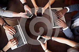 Diverse multiracial people using laptops smartphones on table, t