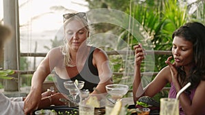 Diverse multiracial women friends sharing food and talking while having dinner. Group of happy multiethnic females