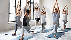 Diverse people doing Warrior one exercise at group yoga lesson