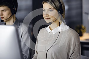 Diverse people group in call center. Blonde business woman talking by headset while sitting in modern office