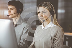 Diverse people group in sunny call center. Blonde business woman talking by headset while sitting in modern office