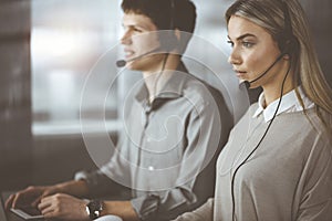 Diverse people group in sunny call center. Blonde business woman talking by headset while sitting in modern office