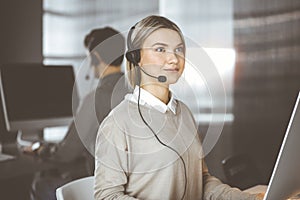 Diverse people group in sunny call center. Blonde business woman talking by headset while sitting in modern office