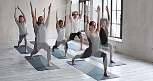 Diverse people practising asana with instructor doing Warrior one asana