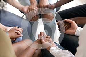 Diverse people sitting in circle holding hands at group therapy photo