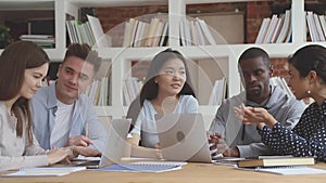 Diverse people sitting at table, studying in groups on computers.