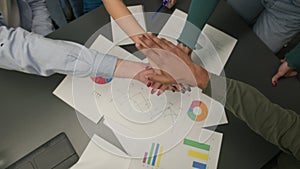 Diverse people women men stacking hands together in pile unite gesture on table with project paperwork group students
