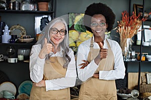 Diverse saleswomen smiling and showing thumbs up at store photo