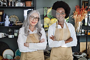 Diverse saleswomen smiling and standing with arms crossed at decor store