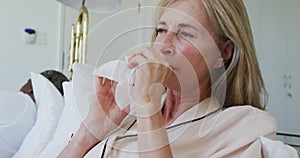 Diverse senior couple in bed woman blowing nose and coughing while man sleeps