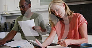 Diverse senior couple using tablet computer paying bills in kitchen