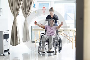 Diverse senior female patient exercising with weights and female doctor advising in hospital room