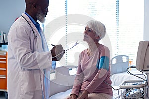 Diverse senior male doctor taking blood pressure of senior female patient in hospital, copy space