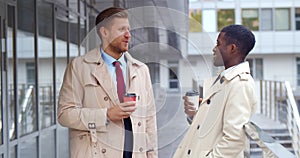 Diverse smiling businessmen with paper cups standing outside office building