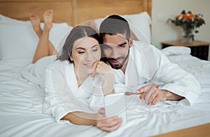 Diverse Spouses Using Cellphone Browsing Internet Lying In Bed Indoors