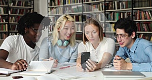 Diverse students groupmates sit in library have fun use cellphone