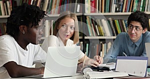 Diverse students sit at desk in library preparing for exams