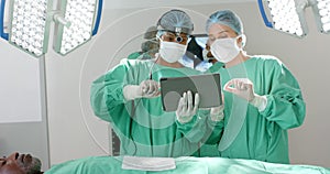 Diverse surgeons wearing surgical gowns, using tablet in operating theatre, slow motion