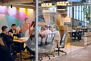 A diverse team of business experts in a modern glass office, attentively listening to a colleague's presentation