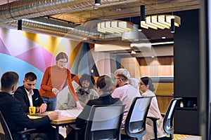 A diverse team of business experts in a modern glass office, attentively listening to a colleague's presentation