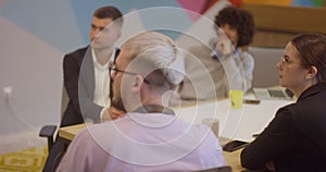 A diverse team of business experts in a modern glass office, attentively listening to a colleague's presentation