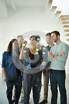 Diverse team of creative designers brainstorming and planning in an office together using sticky notes. Group leader and