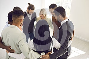 Diverse team of happy young business people standing in office and hugging each other