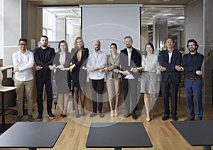 Diverse team of happy corporate employees standing in office, holding hands and smiling