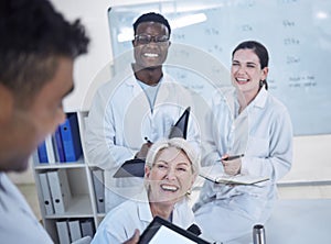 Diverse team of young doctors laughing in lab coats discussing work in laboratory