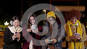 Diverse teenage people having fun together using cell phones on city street