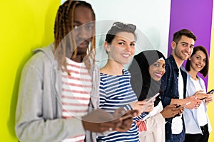 Diverse teenagers use mobile devices while posing for a studio photo in front of a colorful background