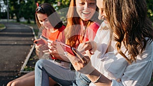 Diverse three girl friends using their phones outdoors. Group gen z young people using mobile smartphone sitting on