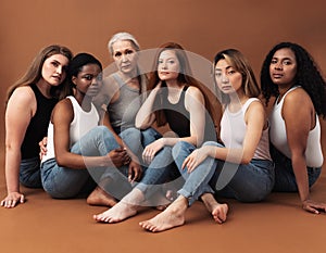Diverse women in casuals sitting on brown background. Multi-ethnic group of females looking at camera in studio photo