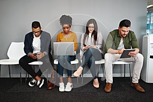 Diverse work candidates sitting in queue in office for job interview using modern gadgets preparing for recruiting