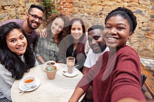 Diverse young friends taking selfies together in a cafe courtyard