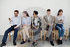 Diverse young people using smartphones while waiting in queue