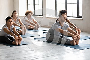 Diverse people doing Seated forward bend exercise, practicing yoga