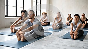 Diverse people practicing yoga with instructor, Seated forward bend exercise