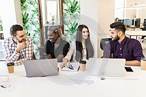 Diverse young and senior office workers collaborating and talking, multiracial employees working on computers. Staff discussing