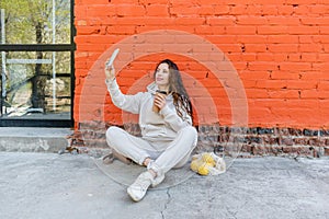 Diversity adult woman, sits on street and drinks coffee from a thermo mug, looks into phone camera and takes selfie.Zero waste