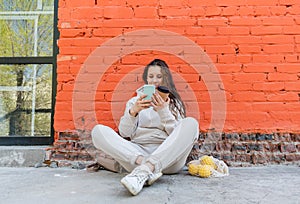 Diversity adult woman, sits on street and drinks coffee from a thermo mug, looks into phone camera and takes selfie.Zero waste