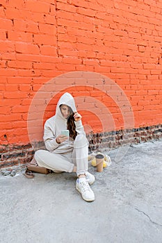 Diversity adult woman, sits on street and drinks coffee from a thermo mug, looks into phone camera and takes selfie.Zero waste