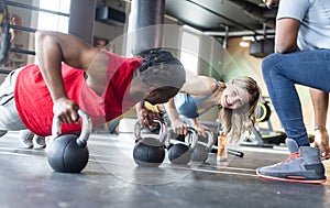 Diversity couple doing push-ups in gym with coach